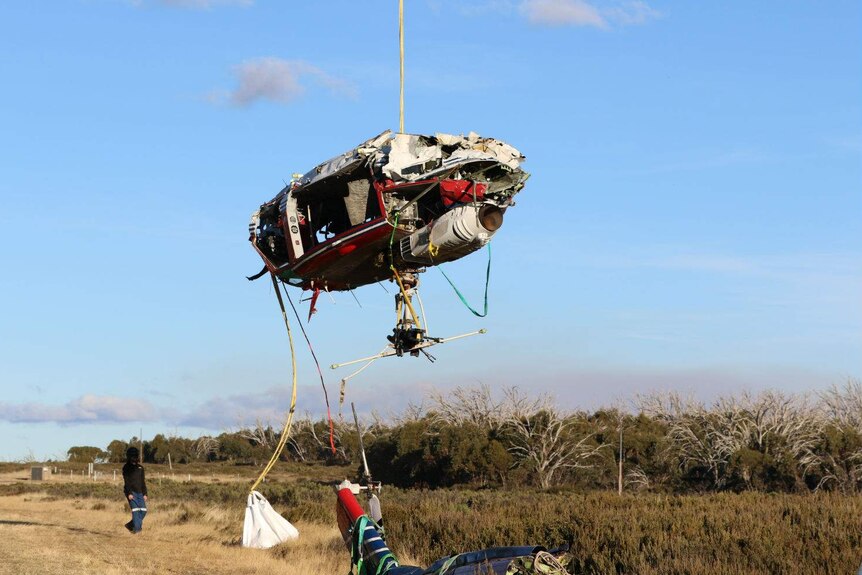 Damaged helicopter suspended from rope in the air.