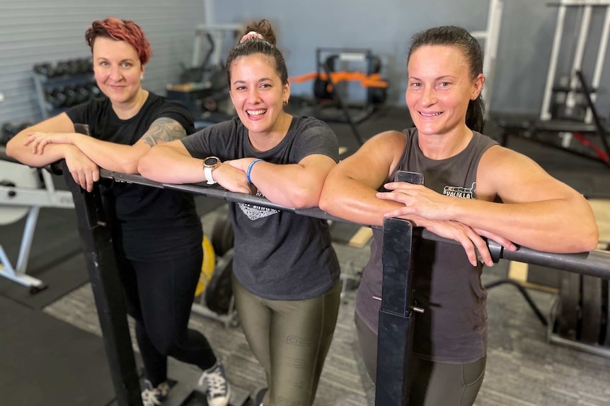 Three women who do weight training smilel in a gym.