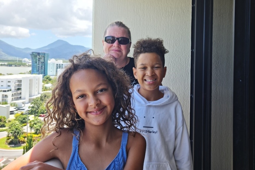 Two children smile at the camera on a hotel balcony, with their Mum standing behind them.