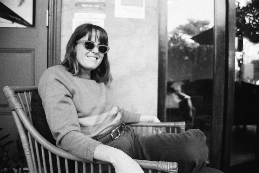 black and white photo of xenica wearing sunglasses sitting in a chair smiling