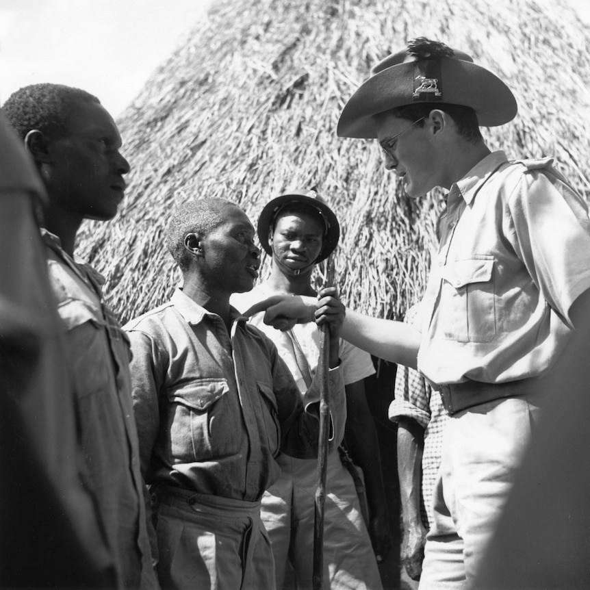 B&W photo of a man in uniform pointing at the chest of an African man, giving orders.