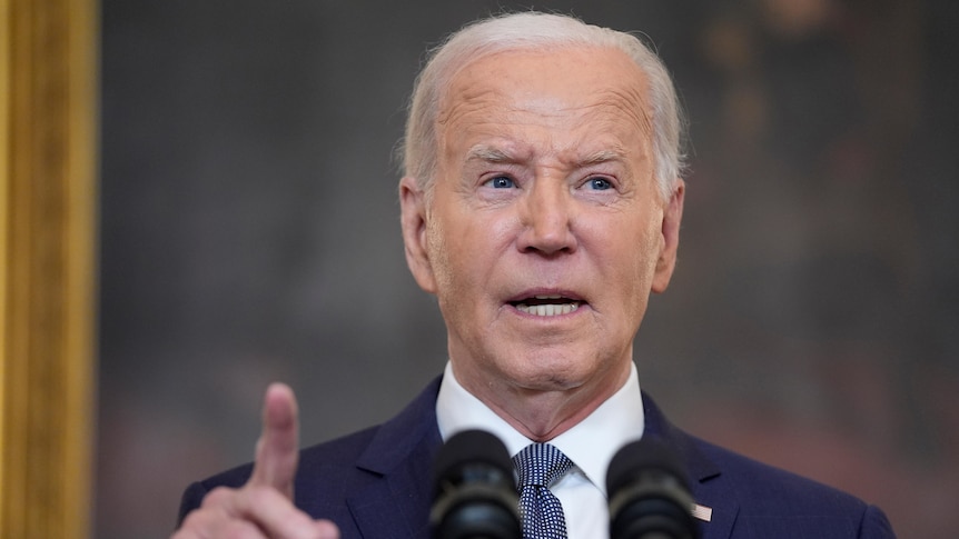 Joe Biden stands behind a lectern speaking with his hand and index finger in the air while making a point