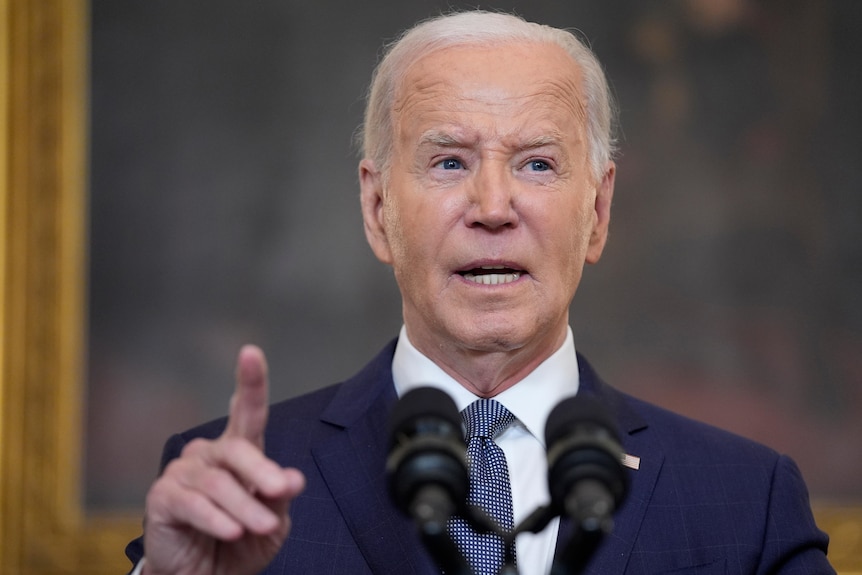Joe Biden stands behind a lectern speaking with his hand and index finger in the air while making a point
