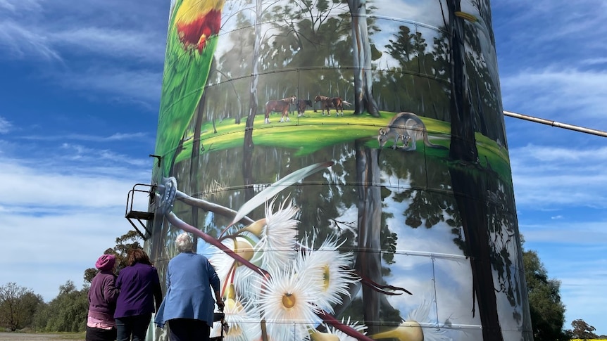 three women looking up at a painted grain silo