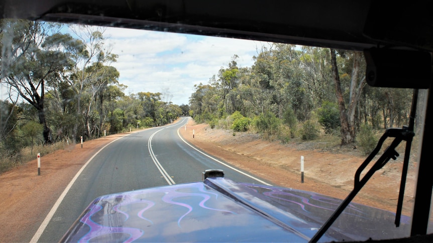 looking out front window of a truck from the cab at a windy empty country road