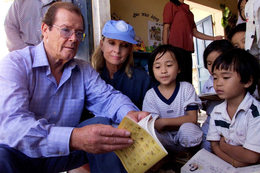 Sir Roger Moore and his wife Kristina Tholstrup read a book to children at a kindergarten in Vietnam.
