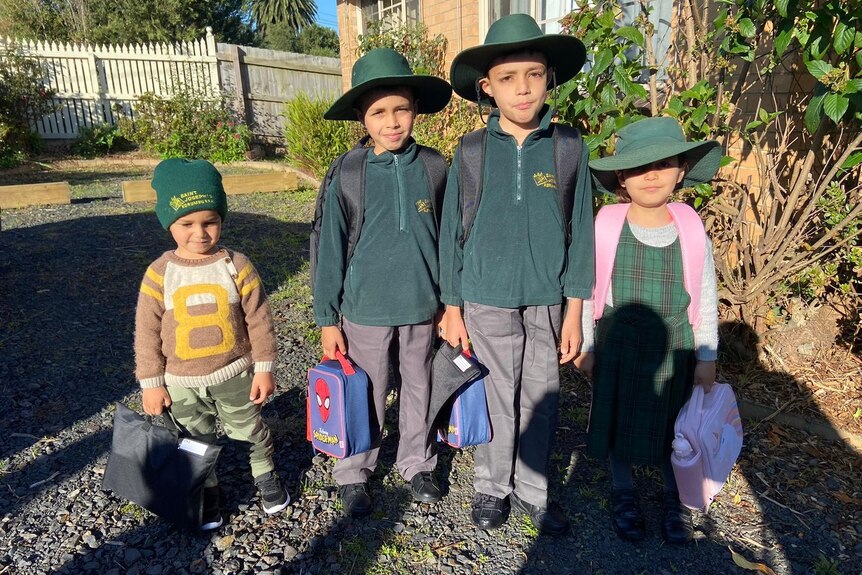 Four children dressed up for school carrying lunch bags