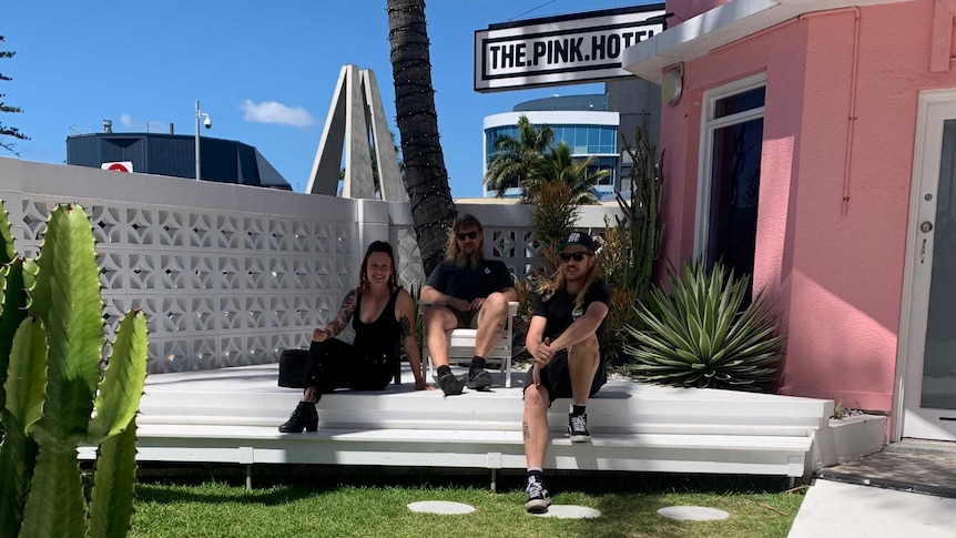 Co-Owners of Pink Hotel Coolangatta Freya Frenzel, Samuel Diklich and Samuel Cleary sitting in hotel grounds.