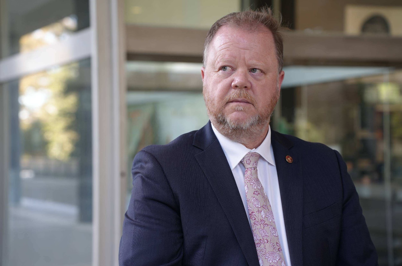 Matthew Swinbourn wears a suit and tie as he delivers a media conference