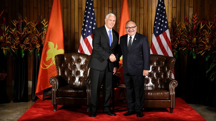 Mike Pence and Peter O'Neill sit on brown leather chairs, in discussion, in front of PNG and US flags.