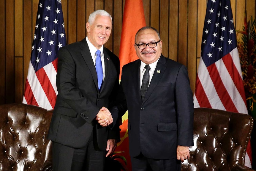 Mike Pence and Peter O'Neill sit on brown leather chairs, in discussion, in front of PNG and US flags.