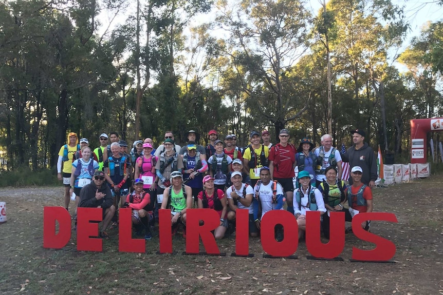 A group of marathon runners and volunteers gather together in the bush for a group photo.