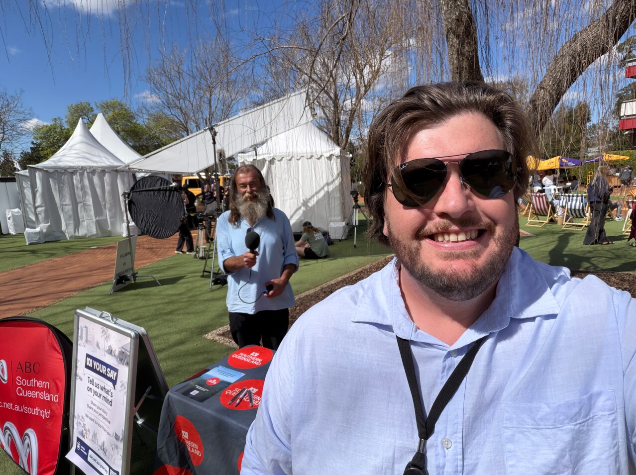 Photo of Saturday presenter Dan Mccray taking a selfie at an abc booth outside, producer Michael Beh behind him