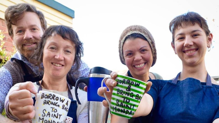 Four staff members from Saint Monday cafe hold reusable mugs to the camera.