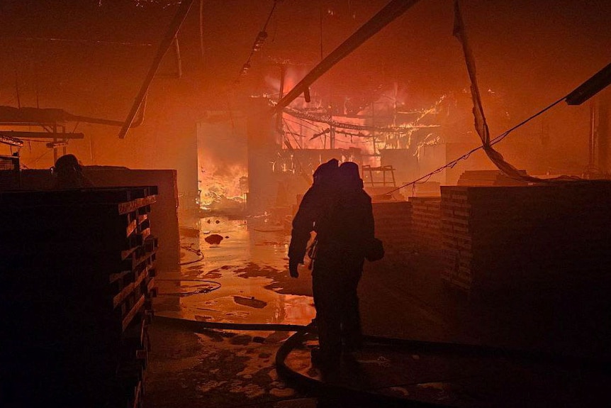 A firefighter walks through a building engulfed in brighht red. 