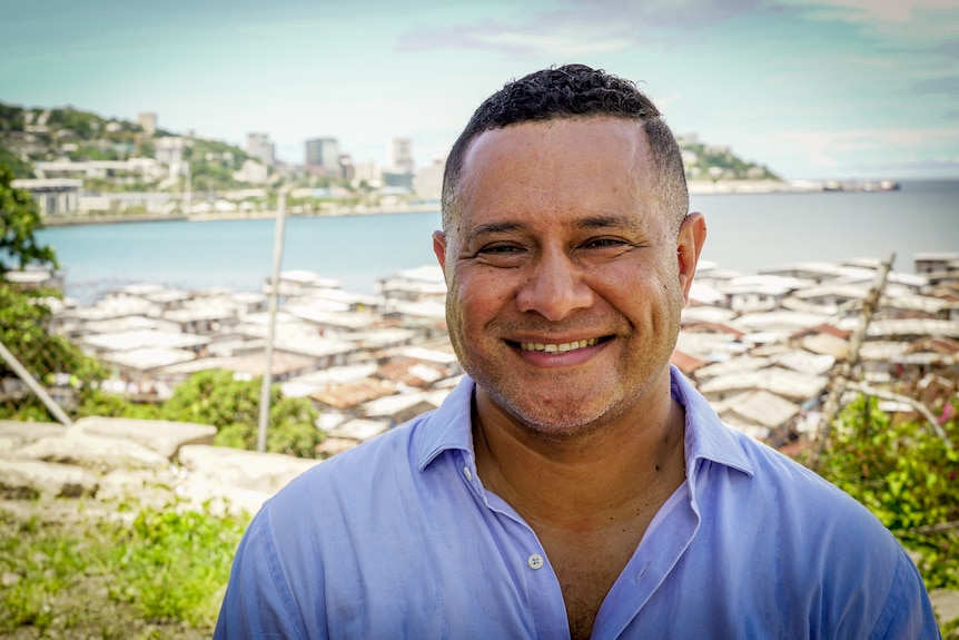 A man in a blue business shirt grins with Port Moresby behind him 
