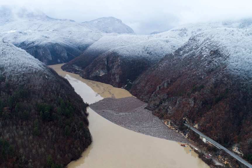 An aerial view of a sectioned off part of a brown river weaving between tall mountains.