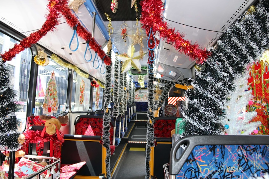 Interior of a bus decorated in masses of colourful tinsel, Christmas trees and other decorations.