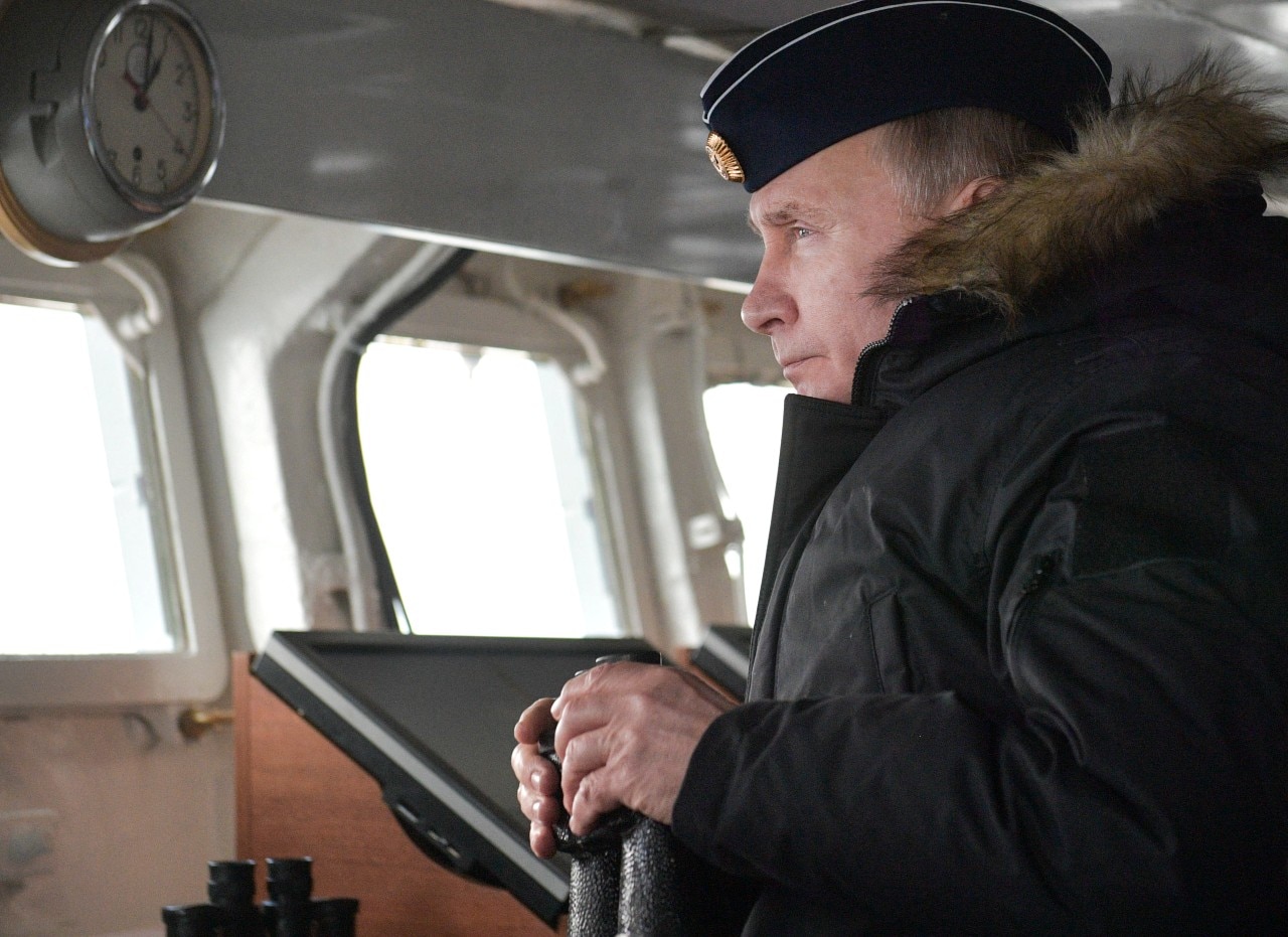 A man inside a ship, wearing a big coat, and looking out to see