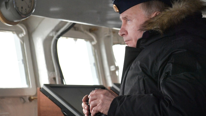 A man inside a ship, wearing a big coat, and looking out to see