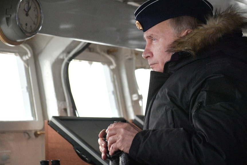A man inside a ship, wearing a big coat, and looking out to see