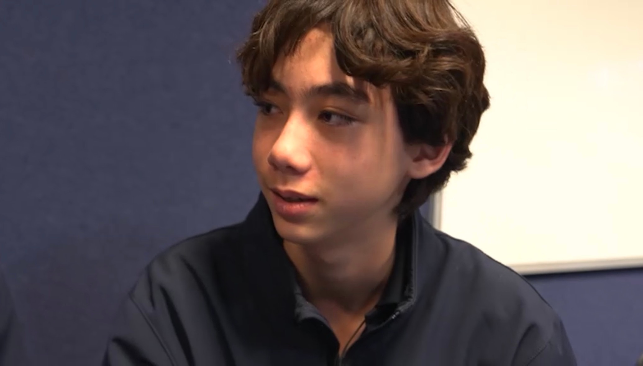 A boy with wavy brown hair looks to the side.