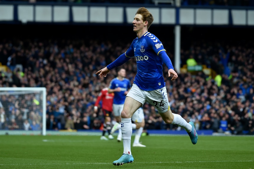 A Premier League footballer jogs toward the stands with arms outstretched in celebration after scoring a goal.