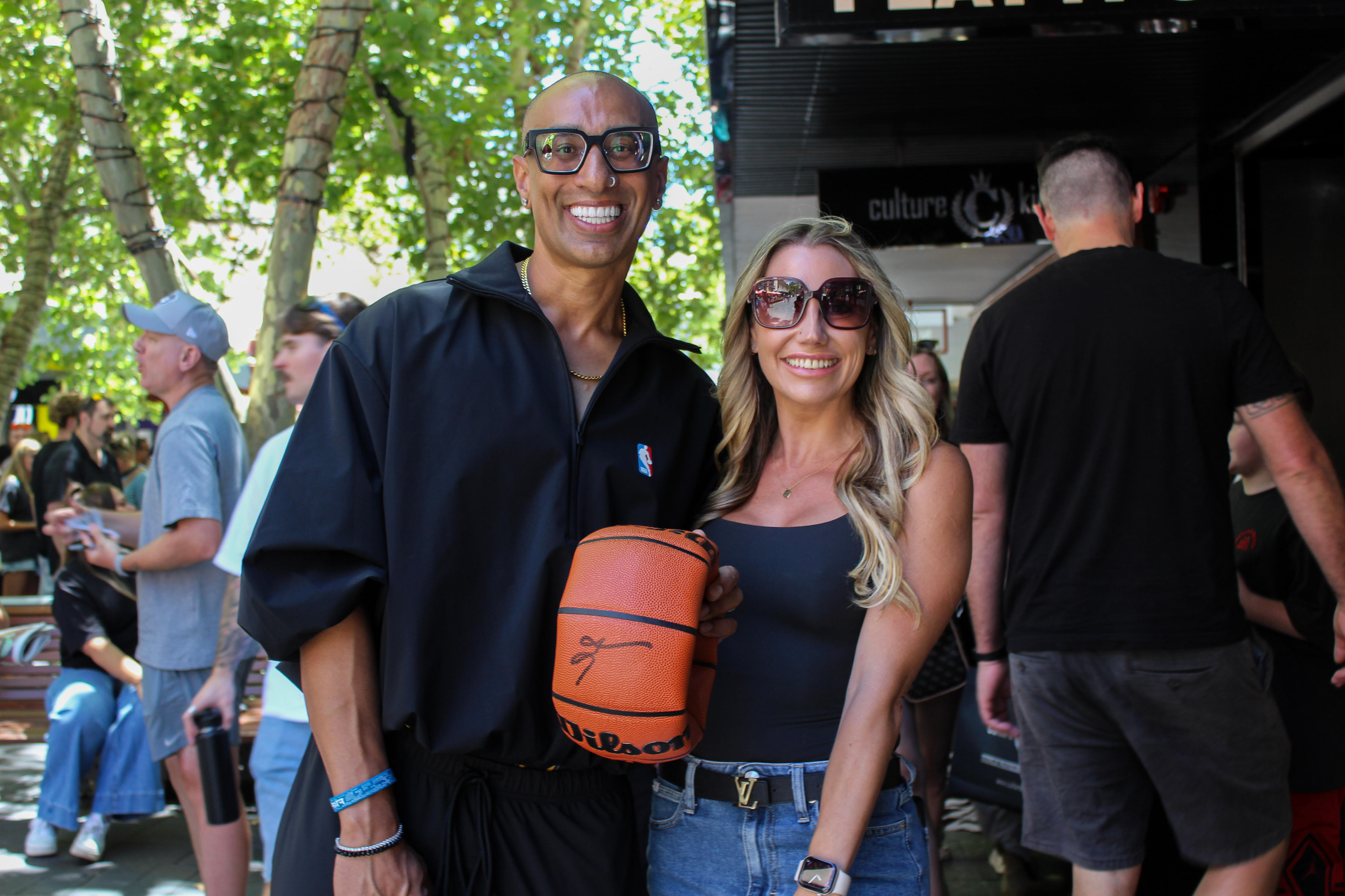 Um homem e uma mulher estão lado a lado sorrindo com uma bola de basquete murcha assinada entre eles.