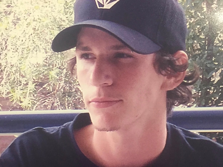 A young man wearing a cap is smiling slightly. 