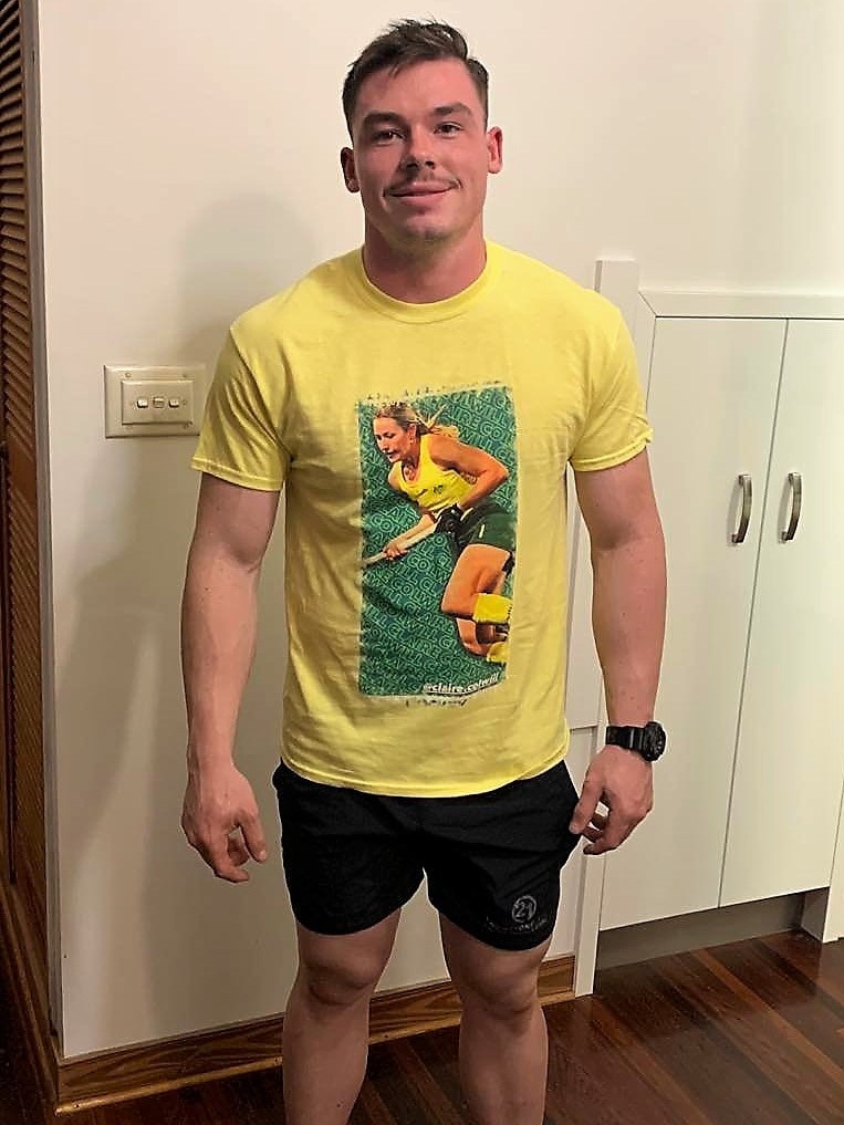 A young man standing in front of a white wall, wearing a yellow shirt with a picture of a hockey player.