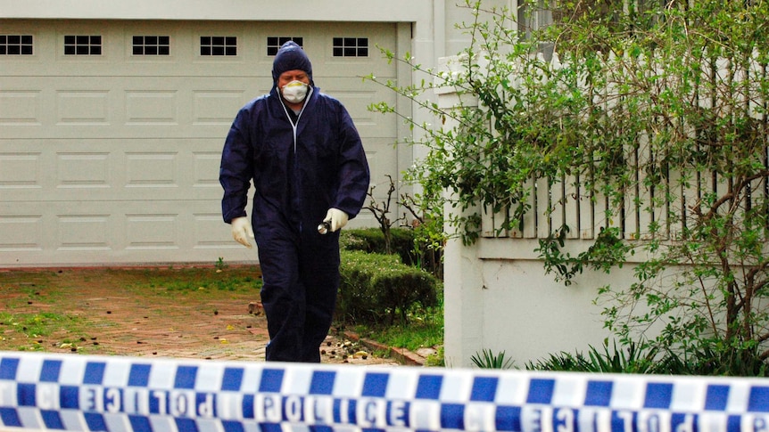 A man in a forensic suit with a face mask, wearing plastic gloves, holding a flashlight, walks out of the Rayney home.