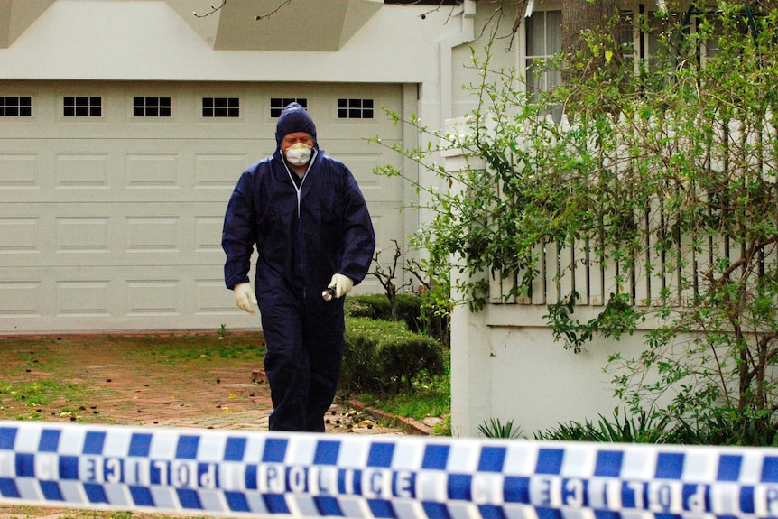 A man in a forensic suit with a face mask, wearing plastic gloves, holding a flashlight, walks out of the Rayney home.