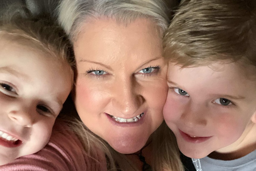 The faces of a woman and her young daughter and son close together, all smiling.