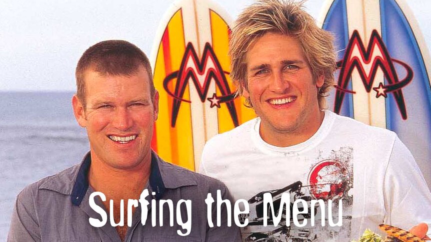 Celebrity chefs Curtis Stone and Ben O’Donoghue posing in front of some surfboards pierced into the sand