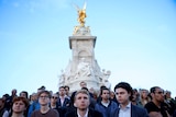 A group of people standing in front of the Victoria Memorial outside Buckingham Palace looking sombre