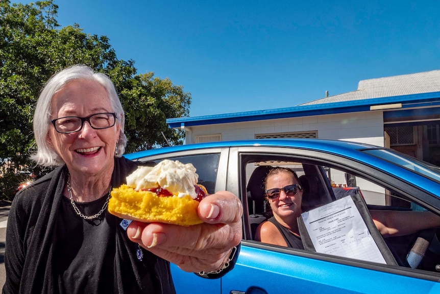 A woman holds a scone as another woman sits in a car.