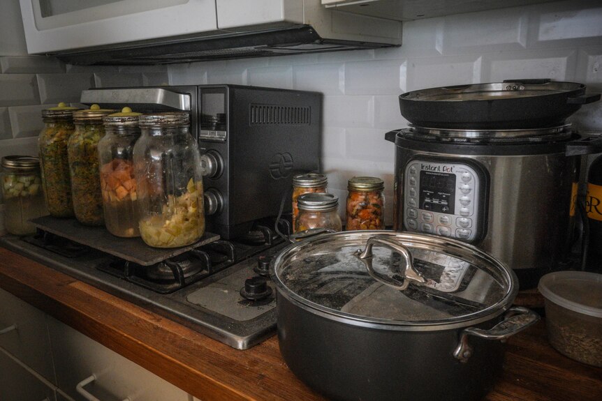jars of fermenting fruits and vegetables sit on a stove top in a kitchen next to unplugged appliances