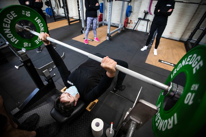 A woman lies on a bench and lifts weights