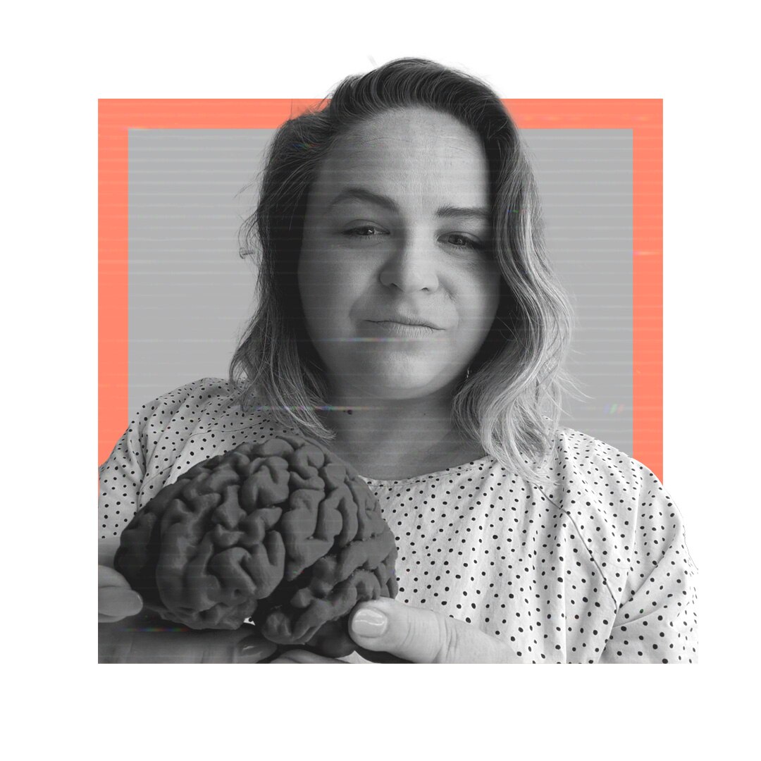 Sarah Hellewell, who has short blonde hair, looks down at a camera holding a model of a brain