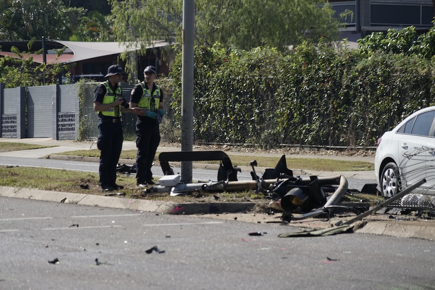 Two police officers standing next to the wreckage of a car
