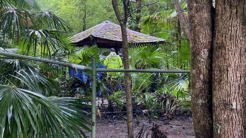 Distant photo of a man in fluro yellow rain jack with 'police' written on it. In amongst scrub and under a gazebo