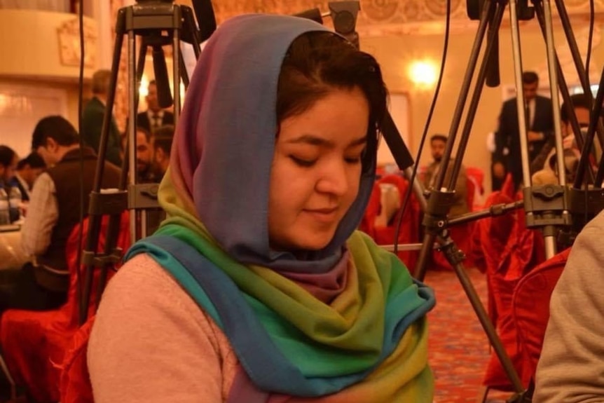 A women wearing a hijab sits with a notebook and pen at a conference.