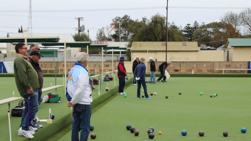 A group of men and women playing bowls outdoors.