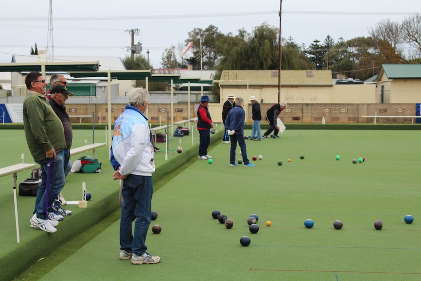 A group of men and women playing bowls outdoors.