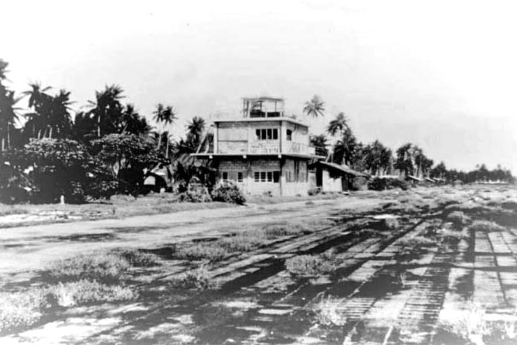 A black and white photo of a tower building next to a row of trees.