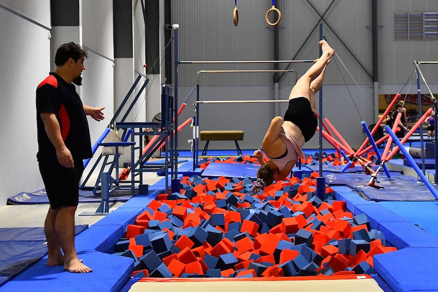 A female twirling upside down into a foam pit with a man looking on from the side
