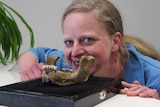 Dr Kristina Eck crouched down and smiling with the jawbone just in front of her jaw