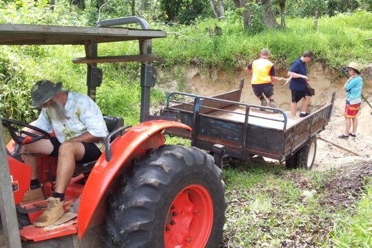 man drives tractor while others look in ditch behind it