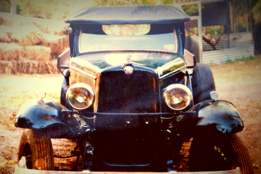 Head-on of an elderly green and black ute. Teardrop headlamps. Haybales. Evening light. Farmyard.