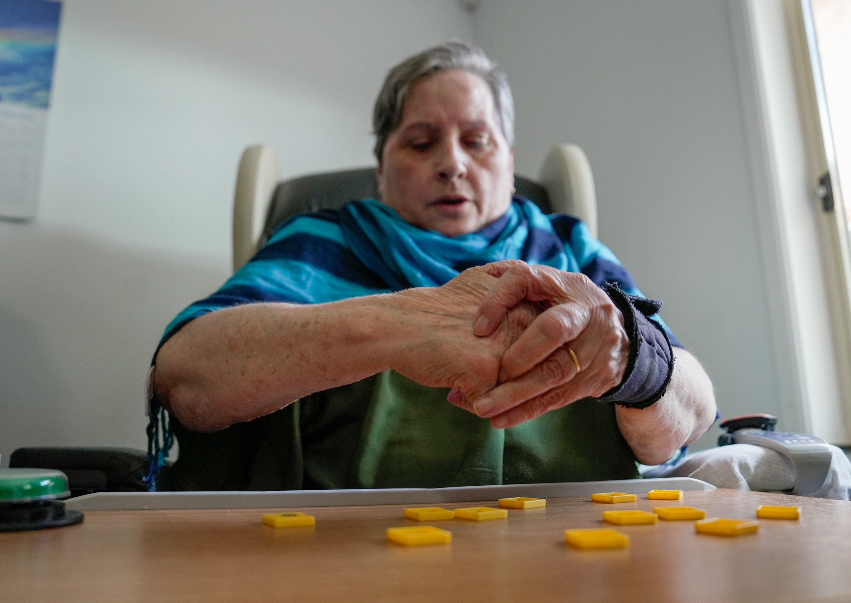 Una mujer blanca de mediana edad se sienta en una silla y se sujeta la muñeca.